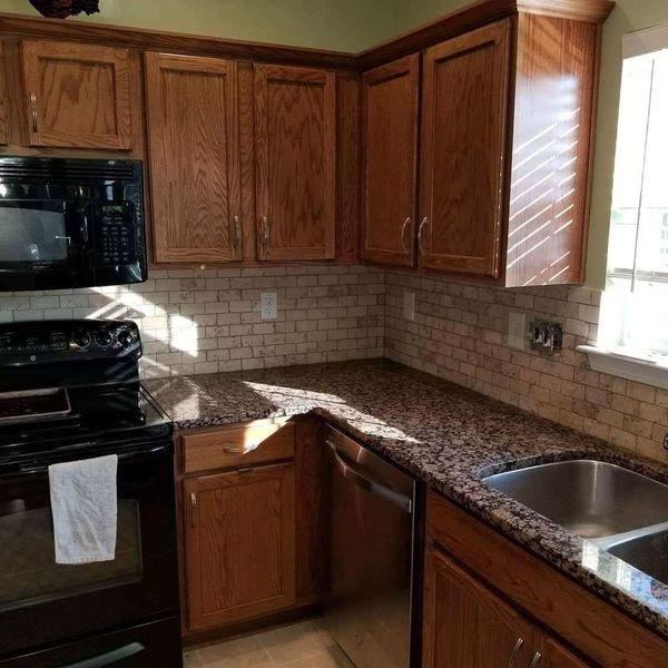 A kitchen with wooden cabinets , granite counter tops , a stove and a sink.