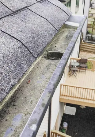 A gutter on the side of a house next to a deck.