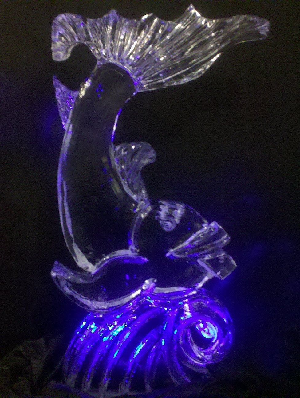 A statue of a dolphin is lit up with purple lights.