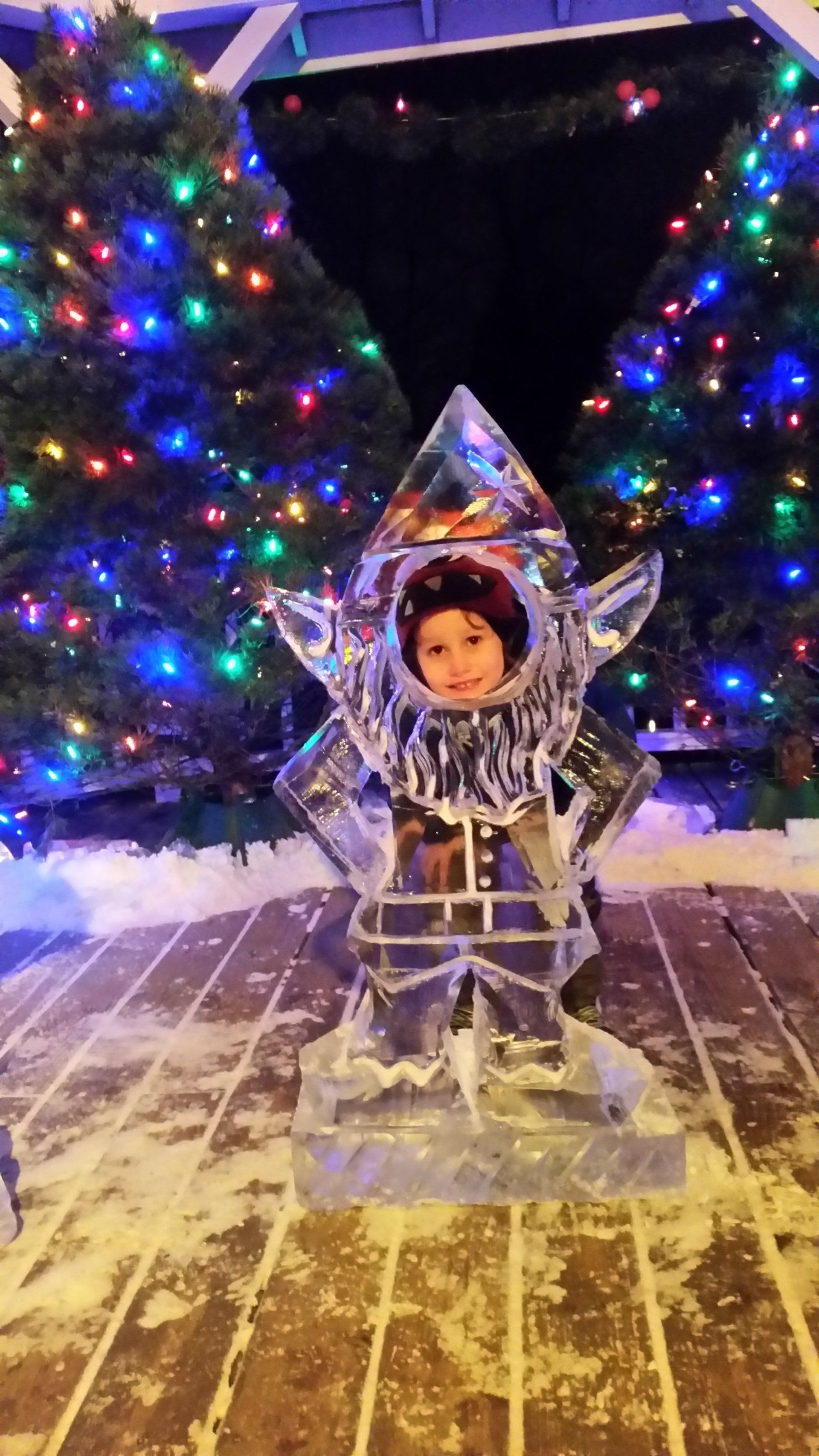 A child is sitting in an ice sculpture in front of a christmas tree.