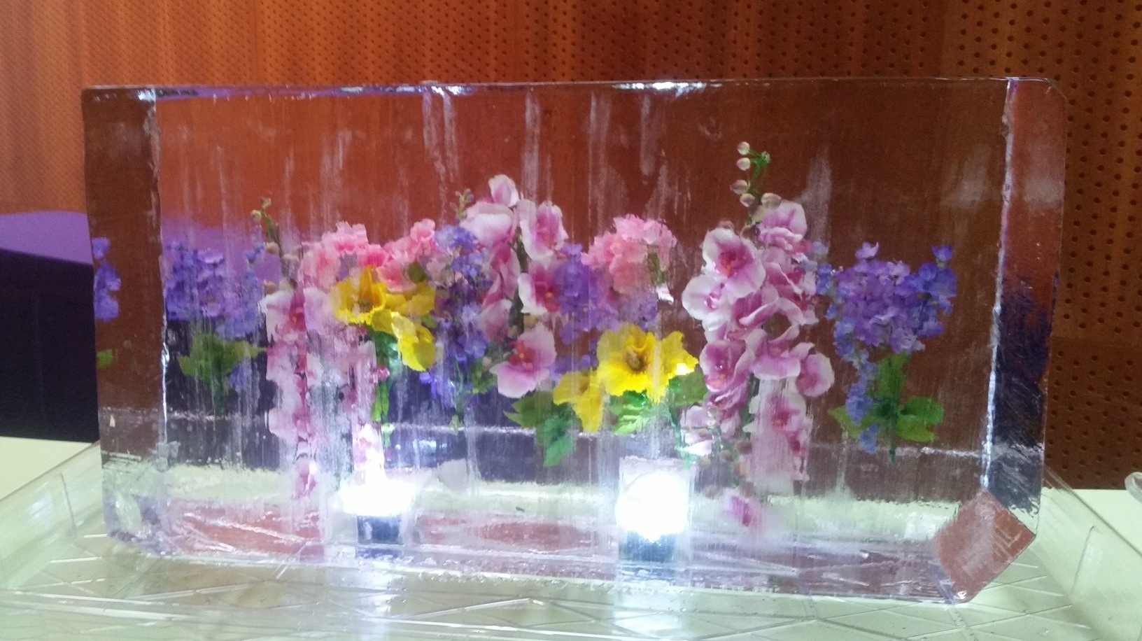 A block of ice with flowers in it is sitting on a table.