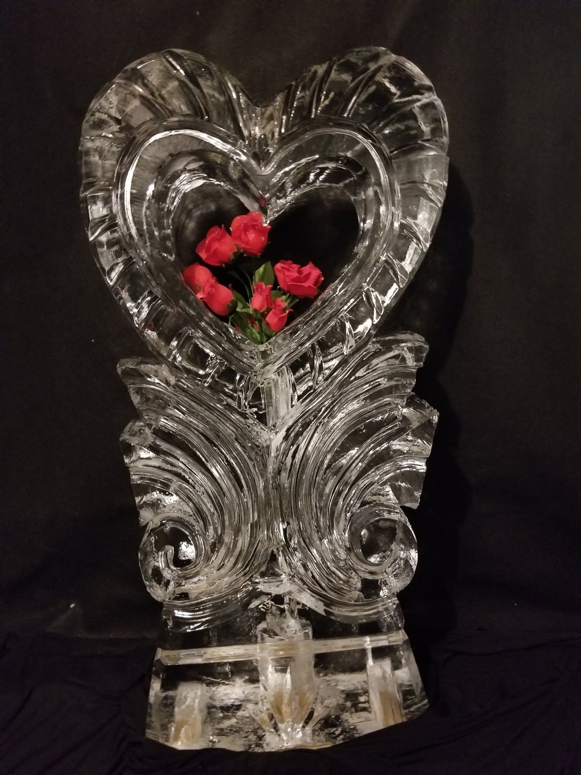 A heart shaped ice sculpture with red roses in it
