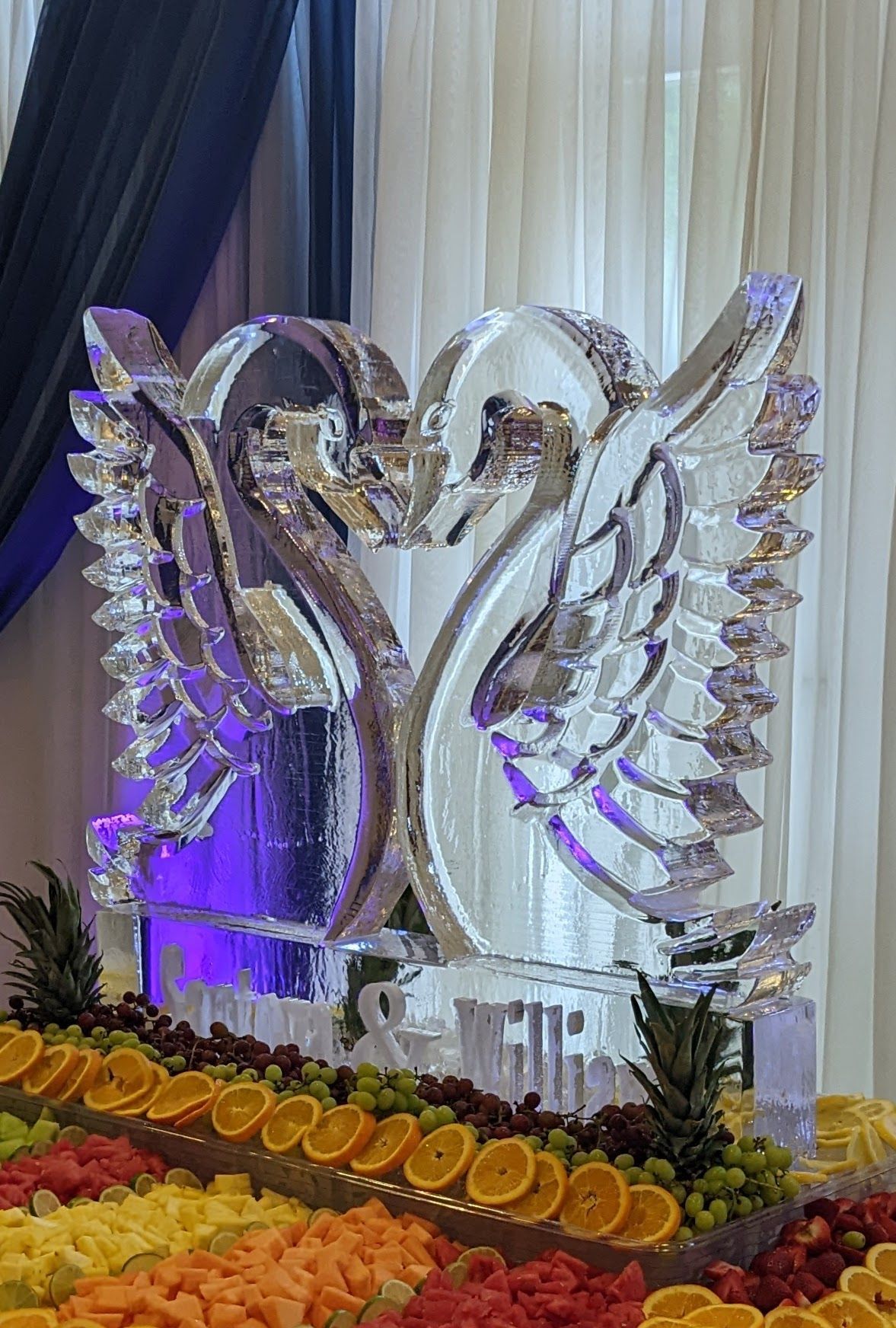 A swan ice sculpture is sitting on top of a fruit display.