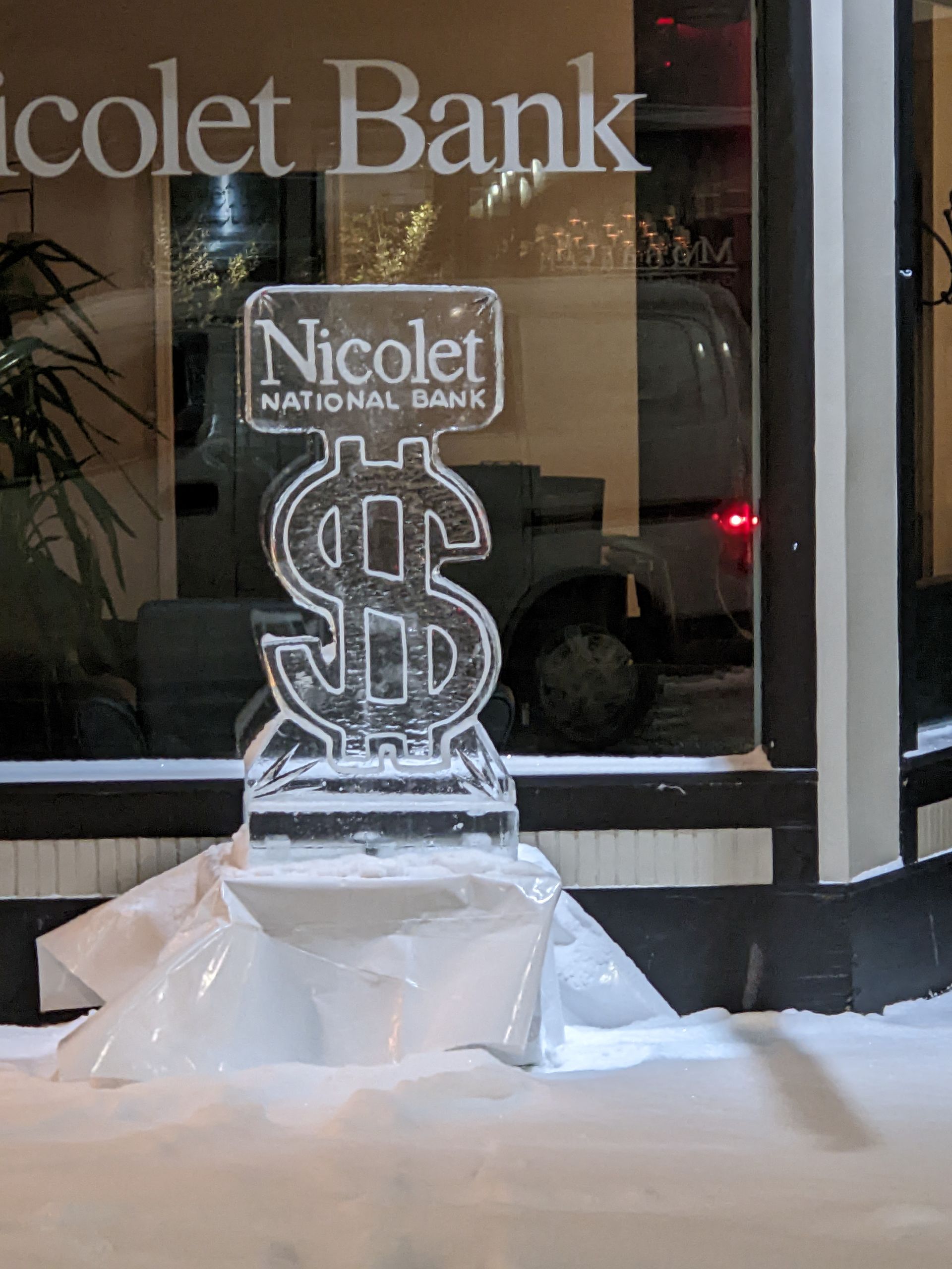 An ice sculpture of a dollar sign is in front of a window.