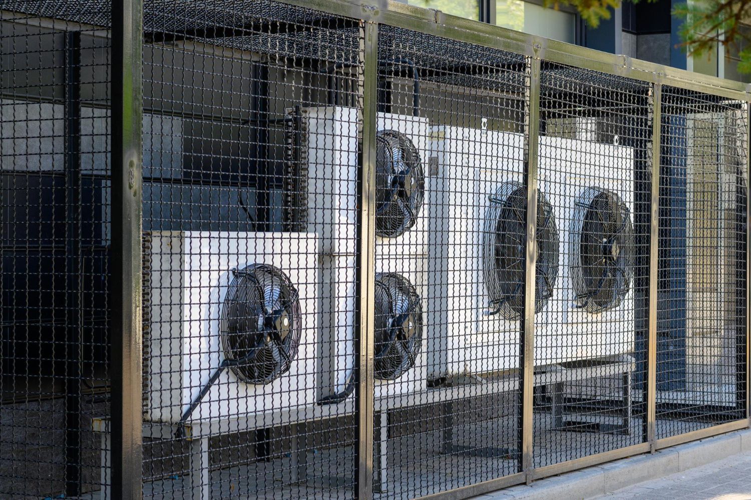 Several industrial outdoor air conditioning condenser units enclosed behind a black metal safety cage.