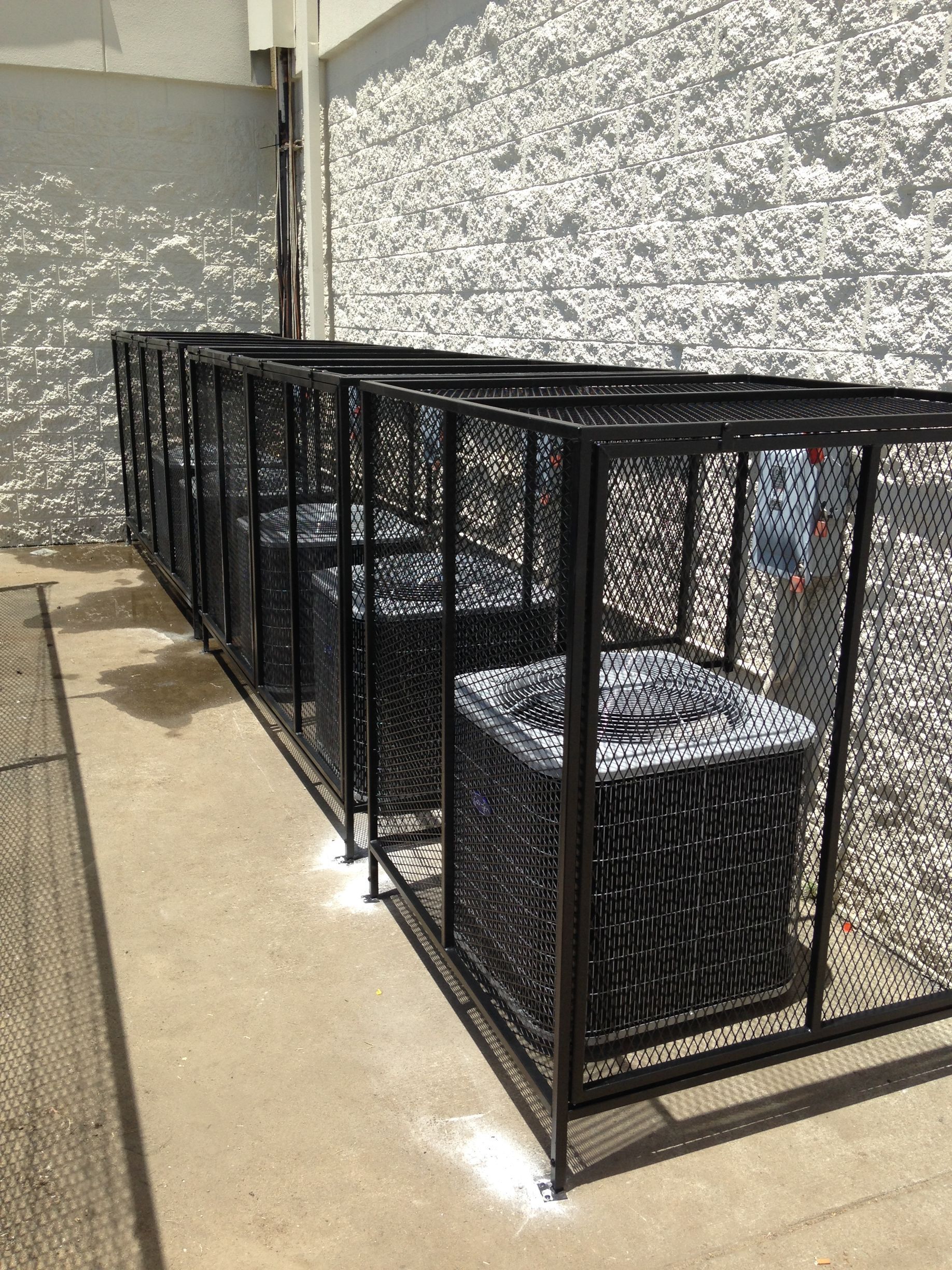 A row of air conditioners are sitting in a cage outside of a building.