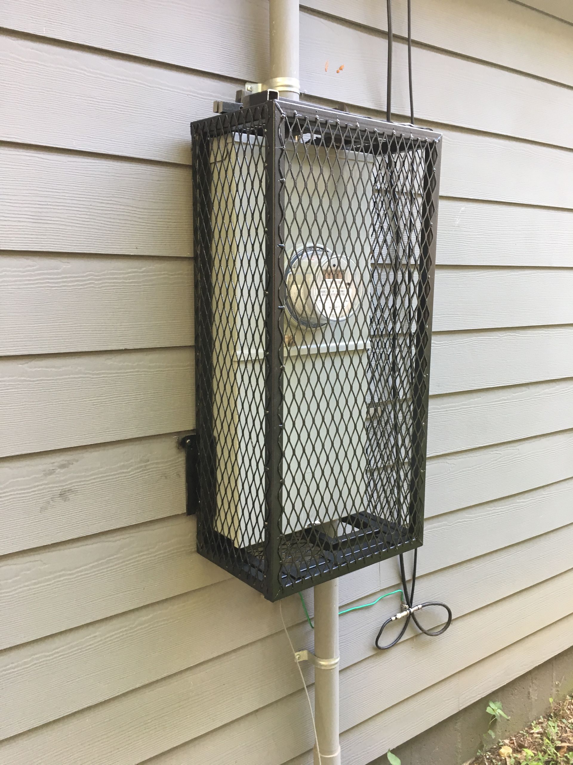 A wire cage is attached to the side of a house.