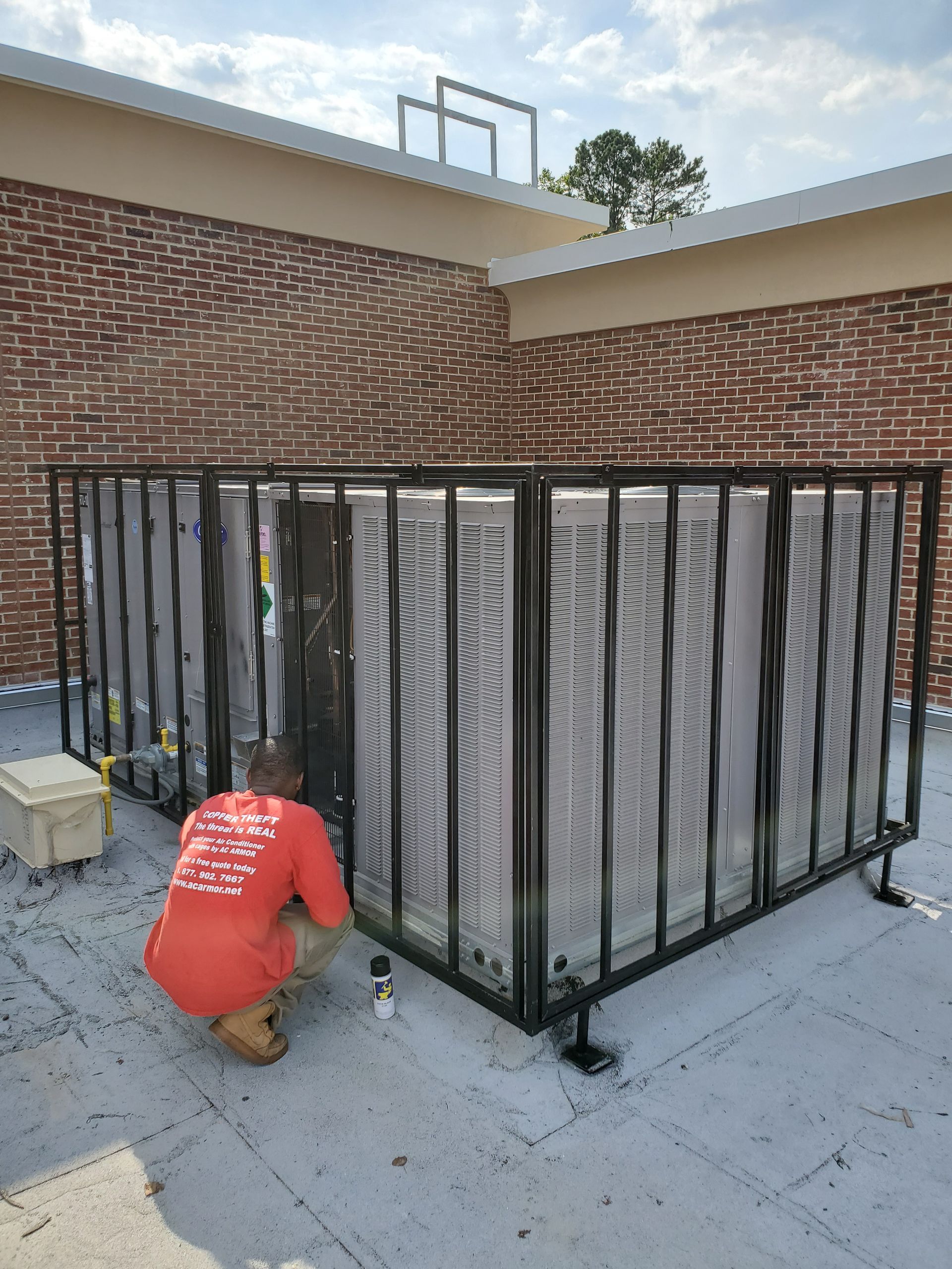 An air conditioner is sitting in a metal cage on the roof of a building.