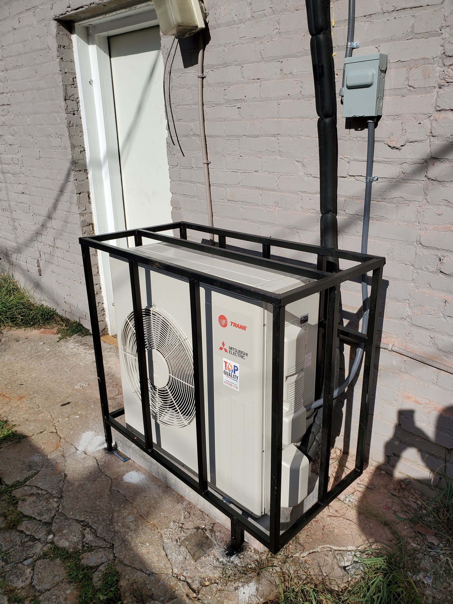 A white air conditioner is sitting in a metal frame on the side of a building.