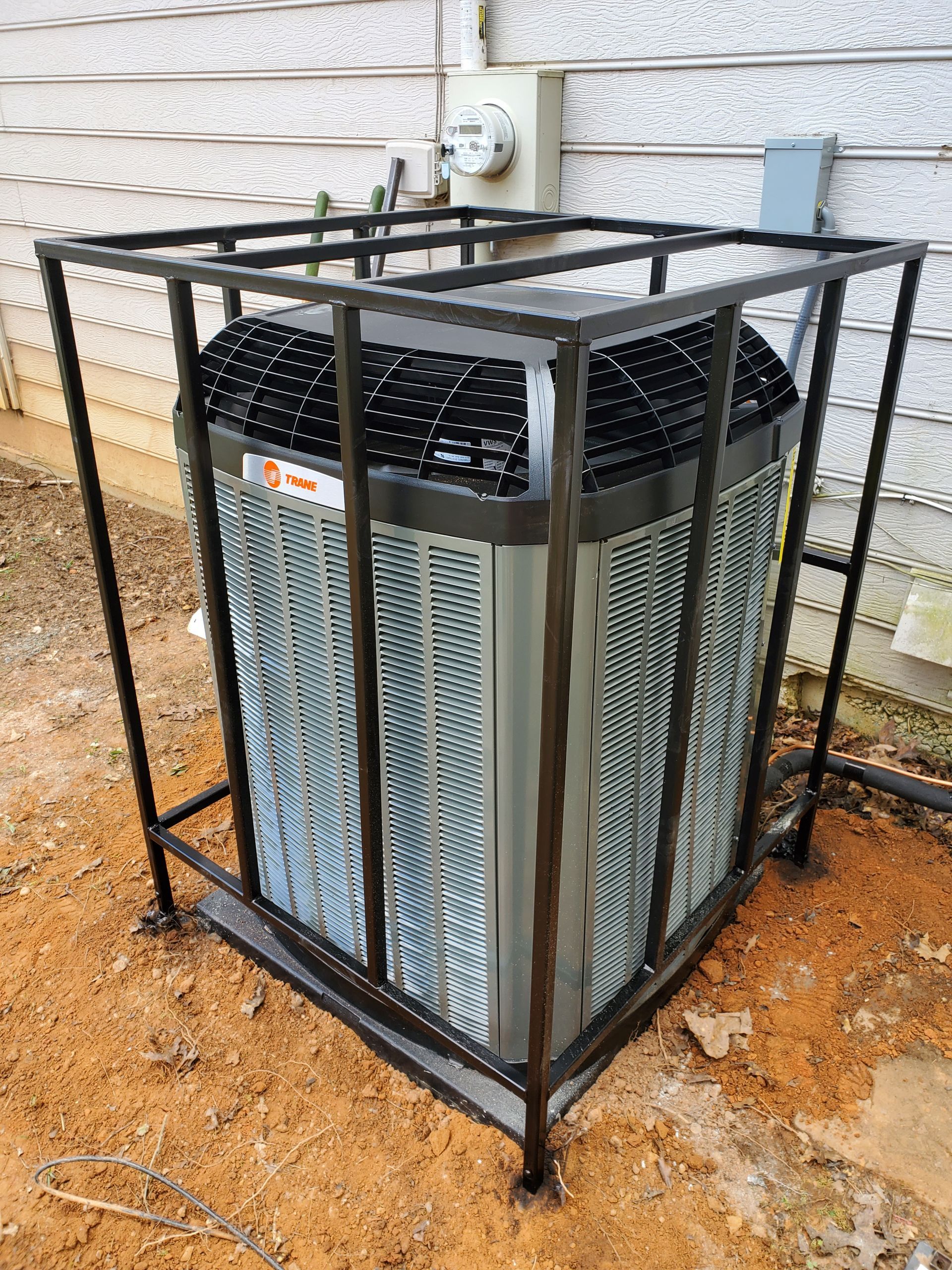 An air conditioner is sitting in a metal cage outside of a house.