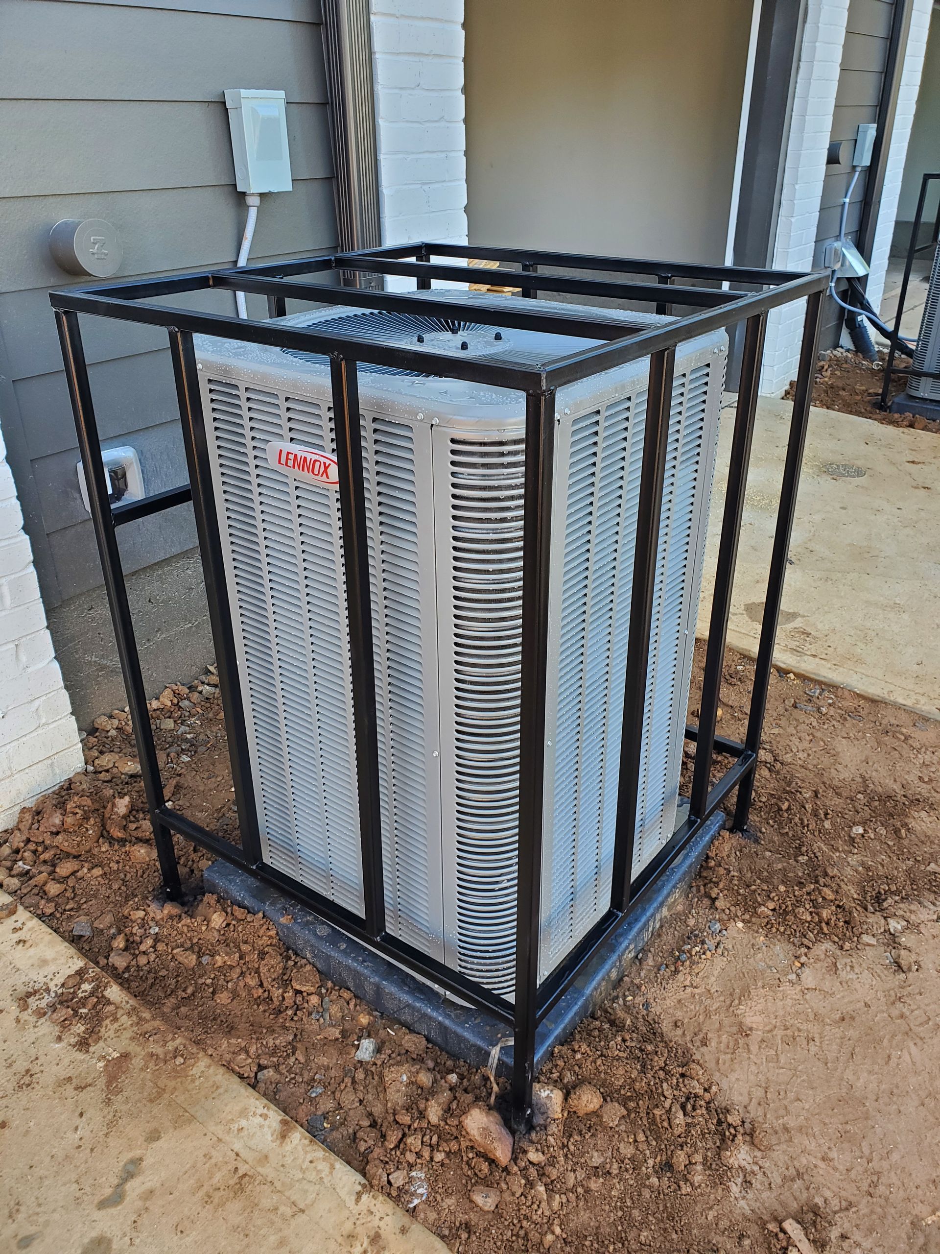 Two air conditioners are sitting next to each other on the side of a house.