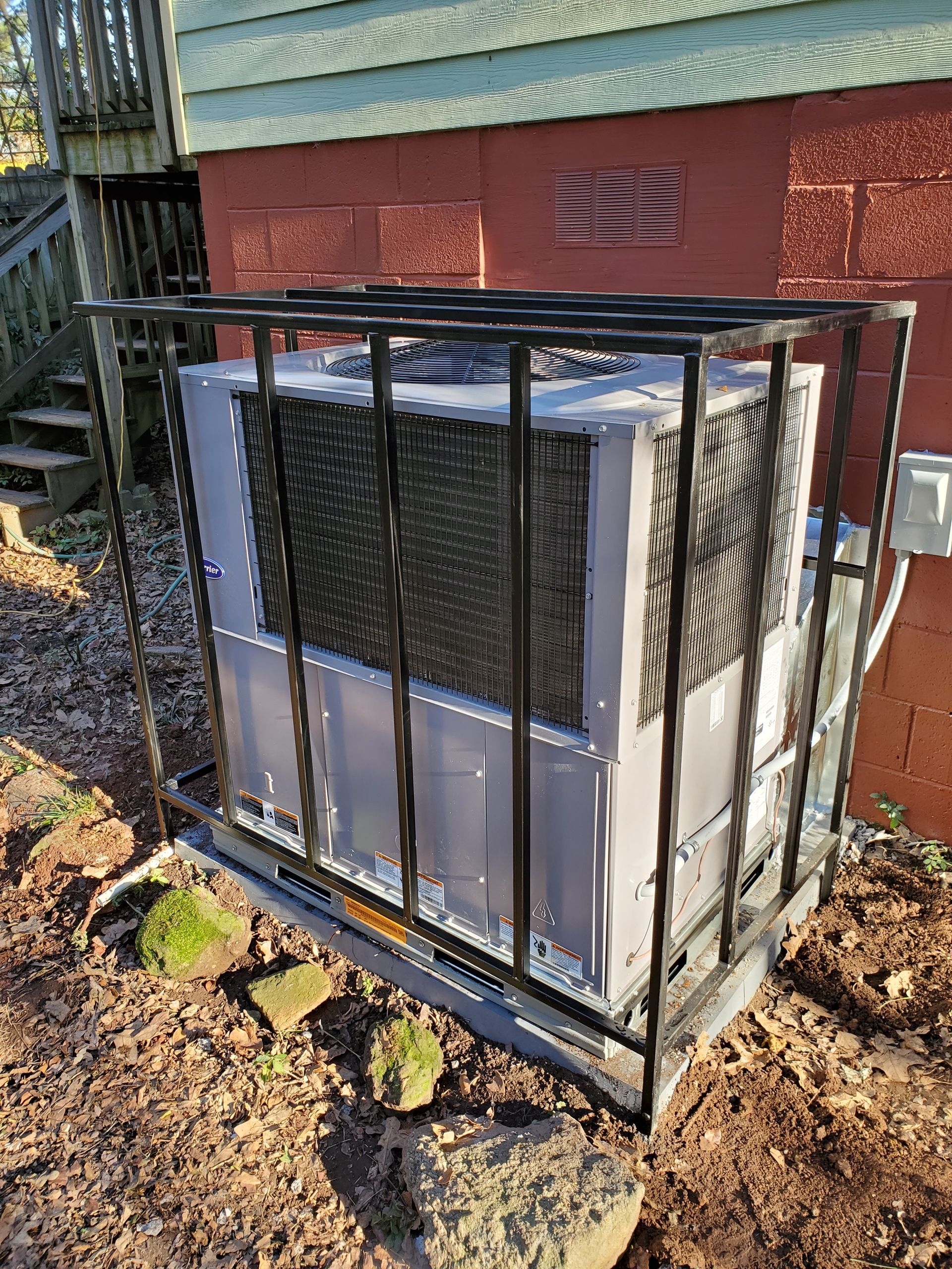 A large air conditioner is sitting in the dirt in front of a house.