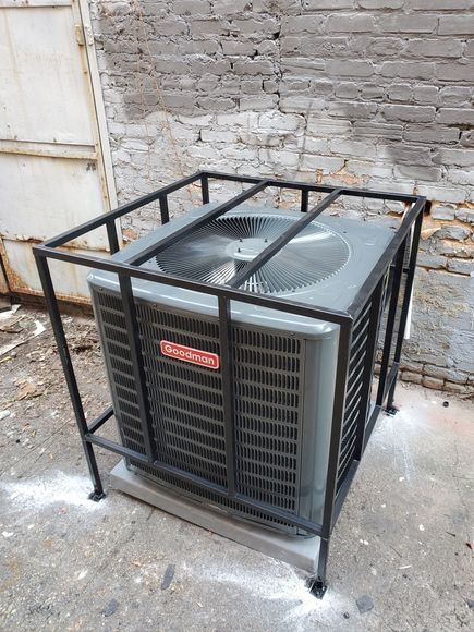An air conditioner is sitting in a metal cage in front of a brick wall.