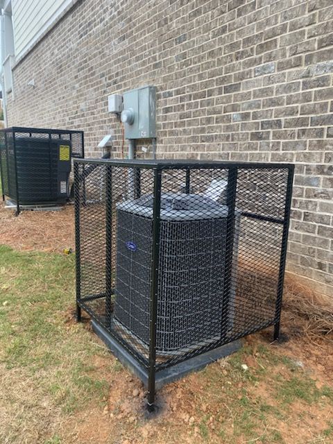 An air conditioner is sitting in a metal cage on the side of a brick building.