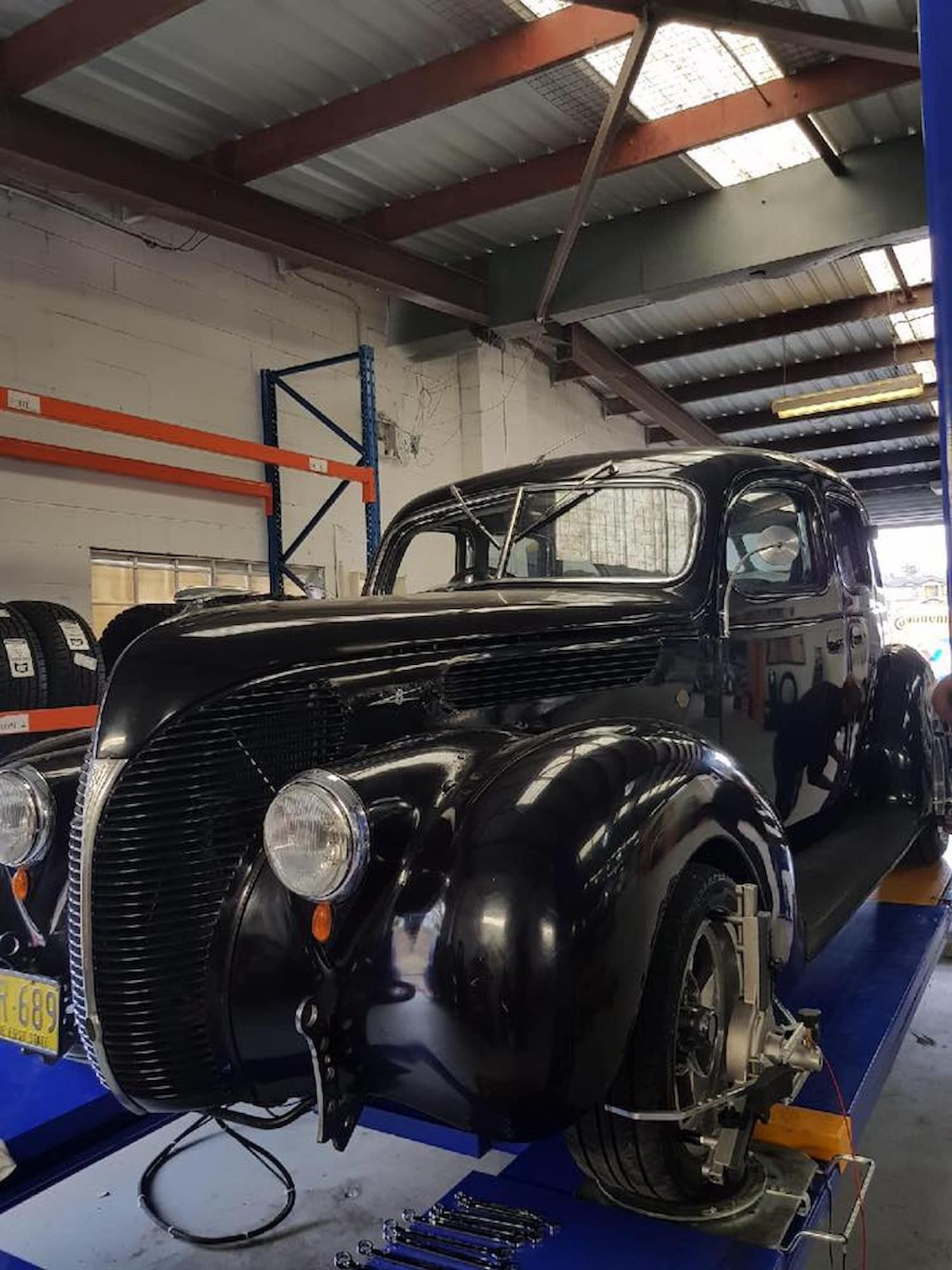 A Black Car Is Sitting On A Lift In A Garage — Sojos Mechanical & Tyre Service In Erina, NSW