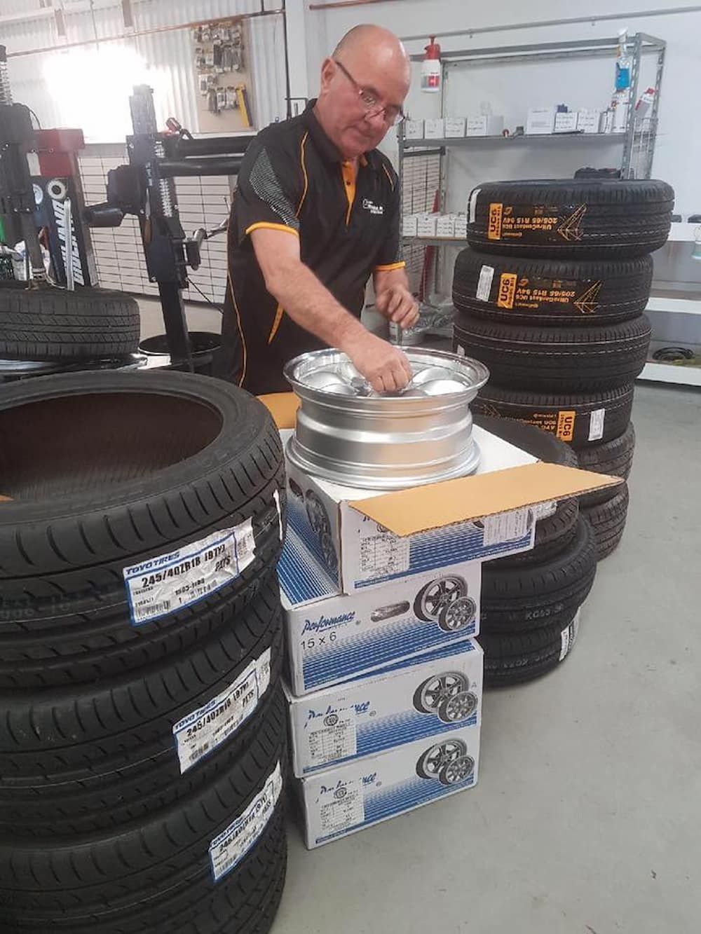 A Man Is Working On A Wheel In A Garage Next To A Pile Of Tires — Sojos Mechanical & Tyre Service In West Gosford, NSW