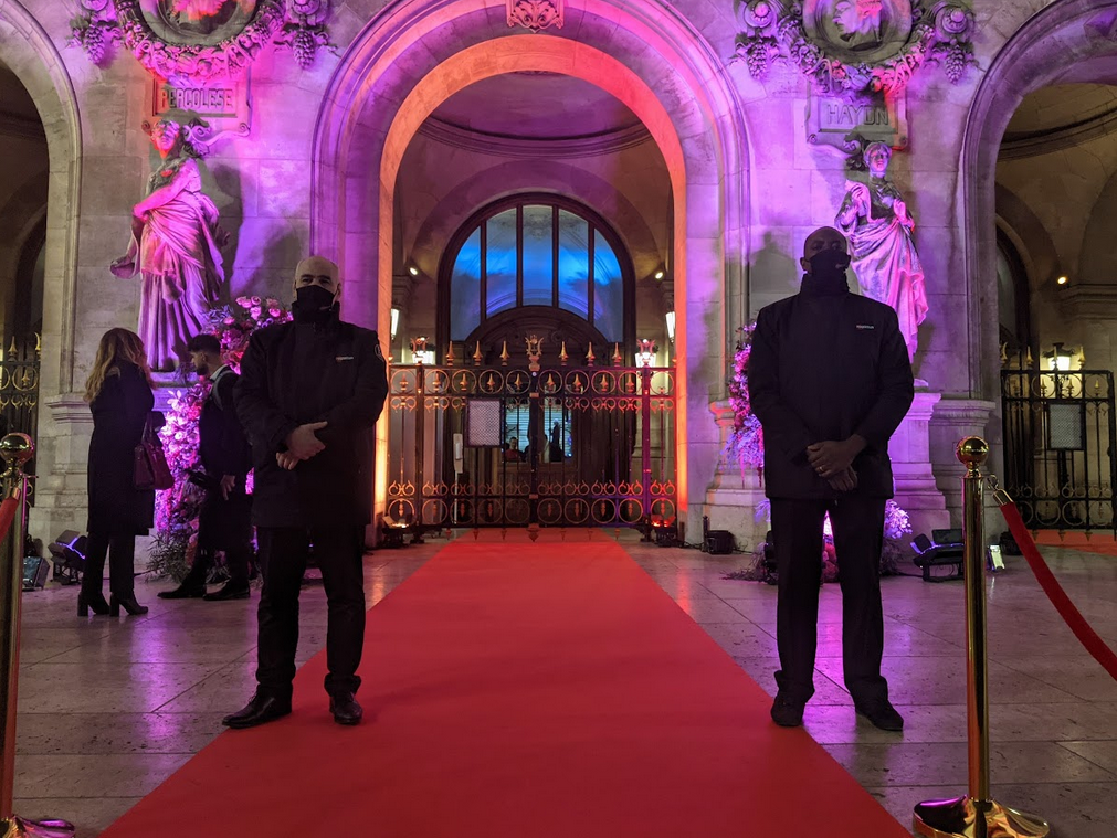 Deux hommes se tiennent sur un tapis rouge devant un bâtiment.