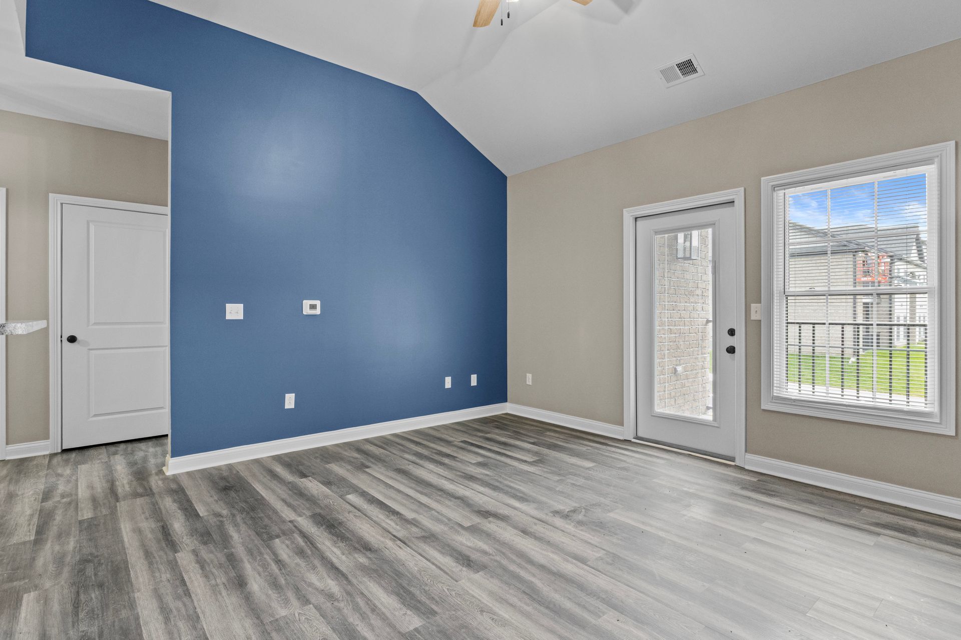 An empty living room with a blue wall , hardwood floors , and a ceiling fan.