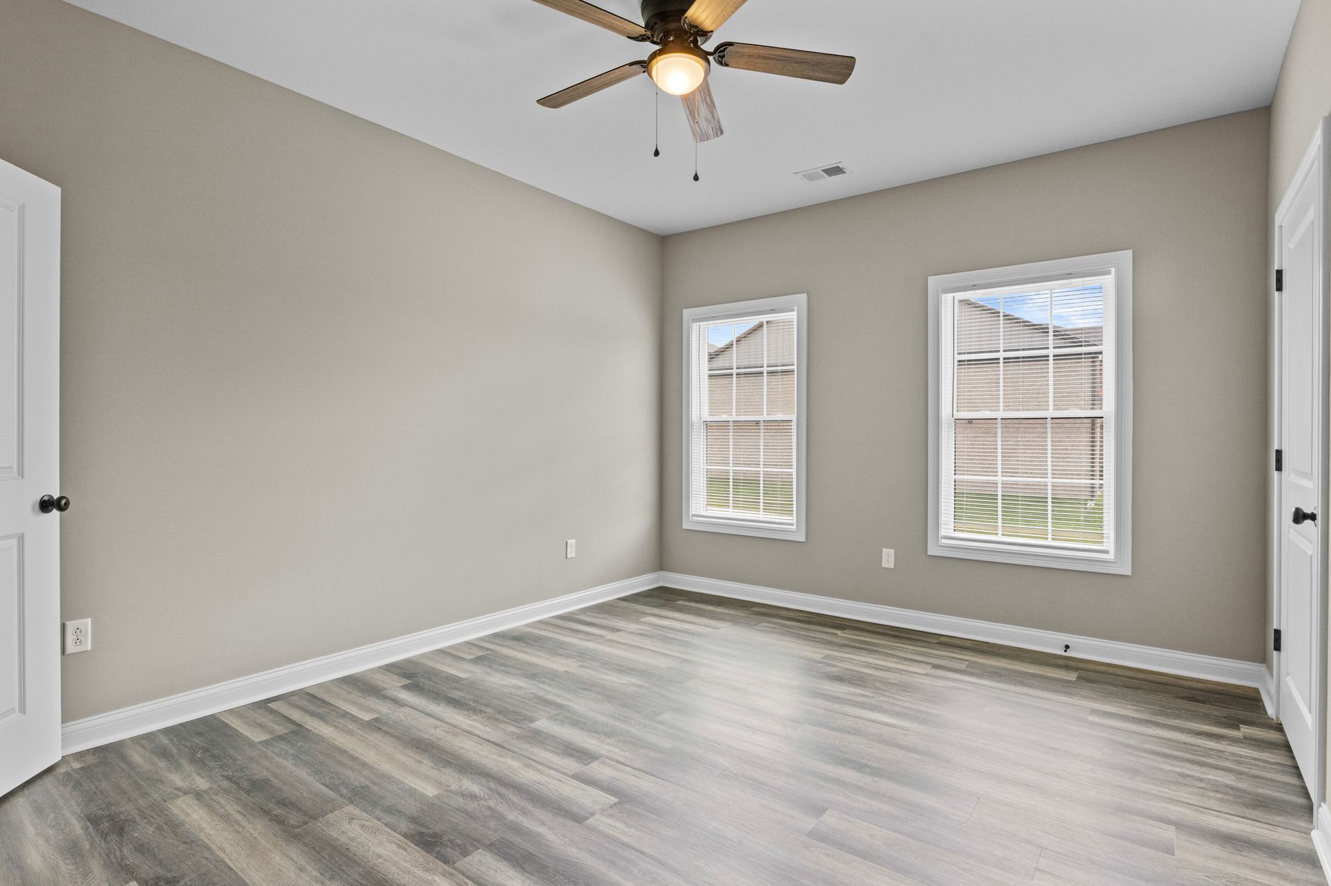 An empty bedroom with a ceiling fan and two windows.