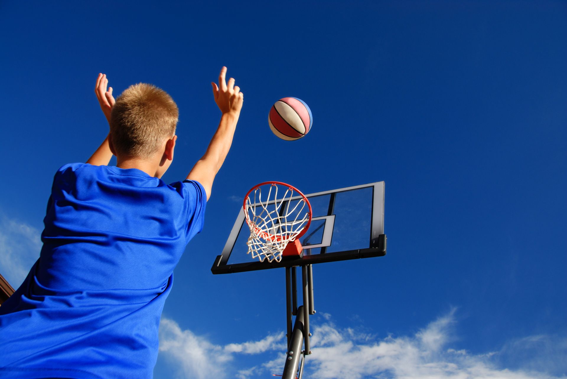 A boy in a blue shirt is throwing a basketball into a basketball hoop.
