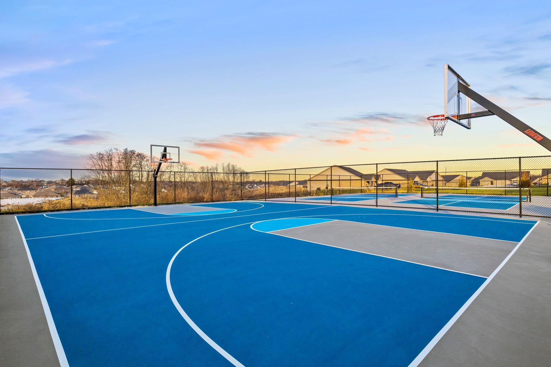 Two tennis courts in a park with trees in the background