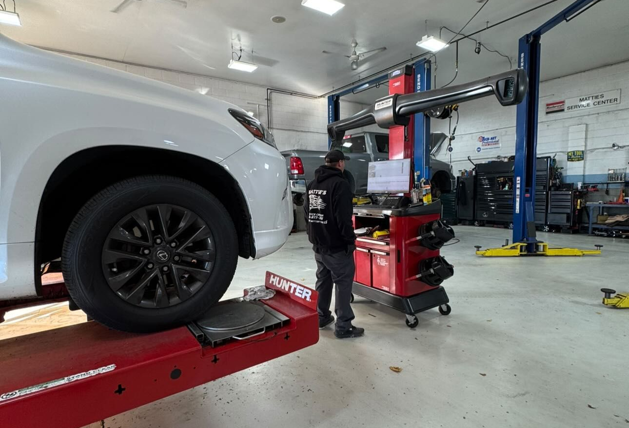 Mechanic in blue overalls inspecting underside of a car on a lift, using a tablet. Garage setting.