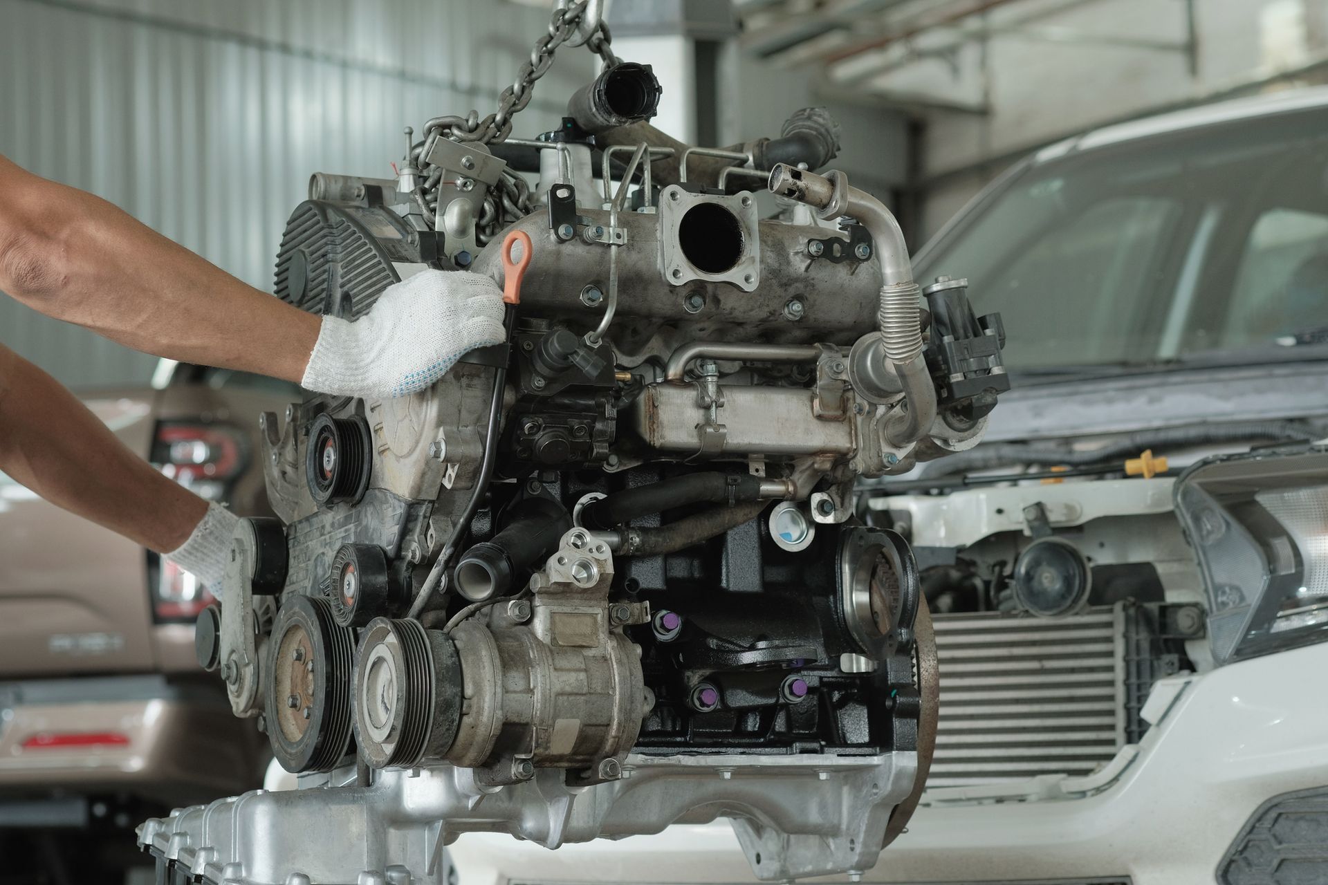 An unrecognized mechanic prepares a repaired car engine for installation at an auto shop.