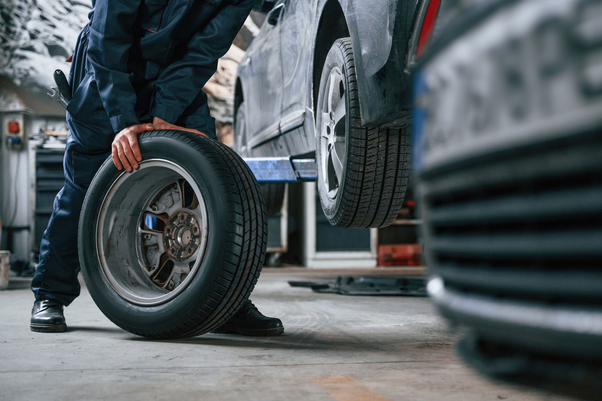 Auto technician removing car wheel during tire service in repair shop garage setting environment