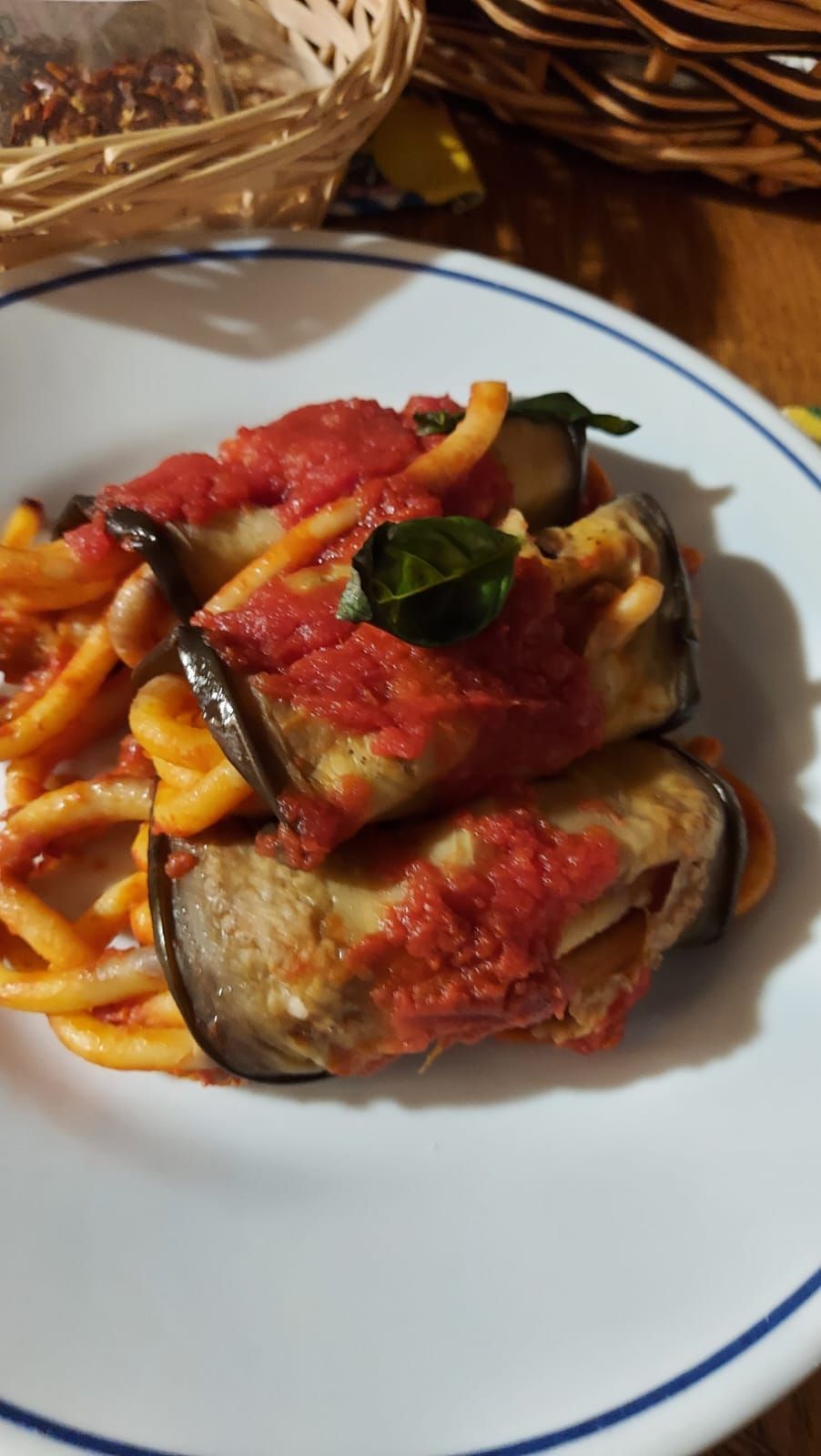 un piatto bianco condito con tagliatelle, melanzane e salsa di pomodoro.