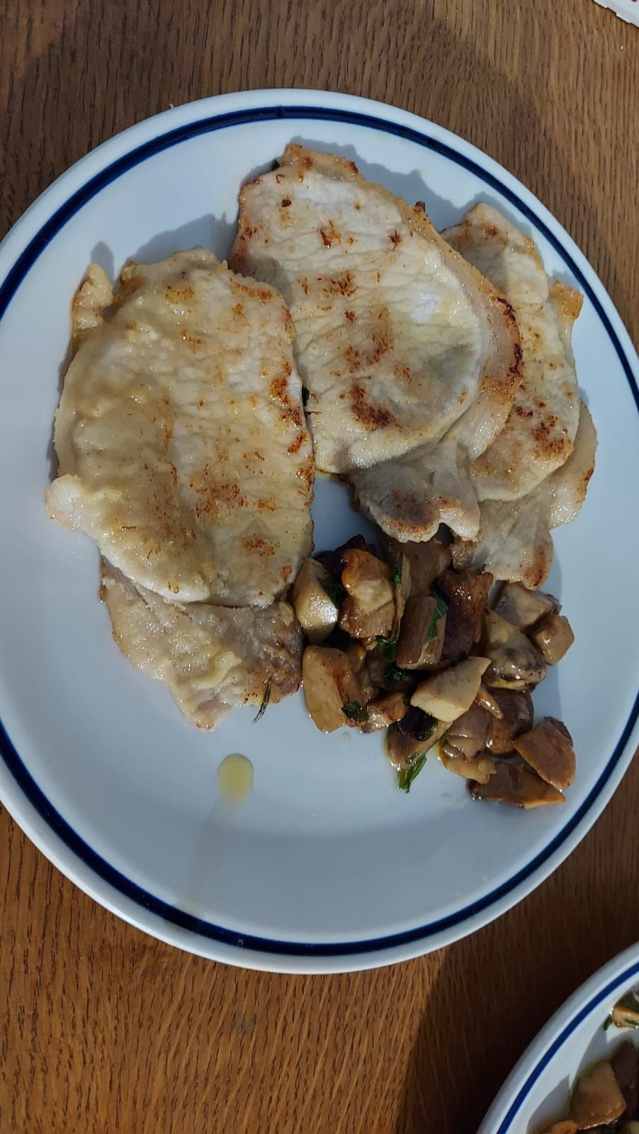 un piatto bianco condito con carne e funghi su un tavolo di legno.