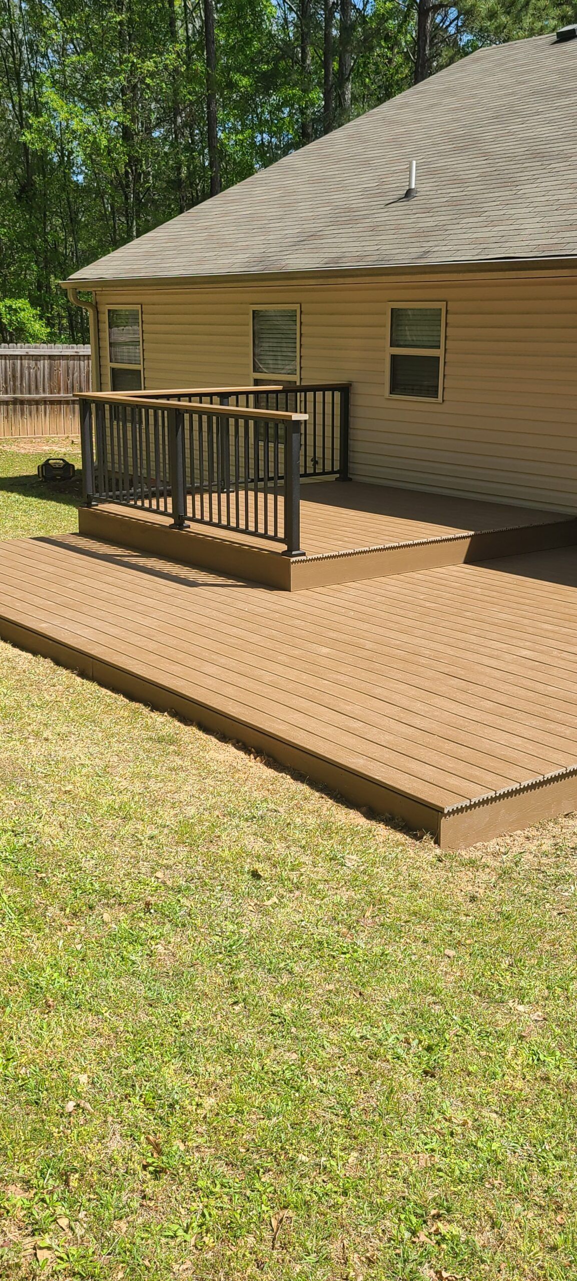 A backyard deck made of brown wood, with a house in the background and a grassy lawn.