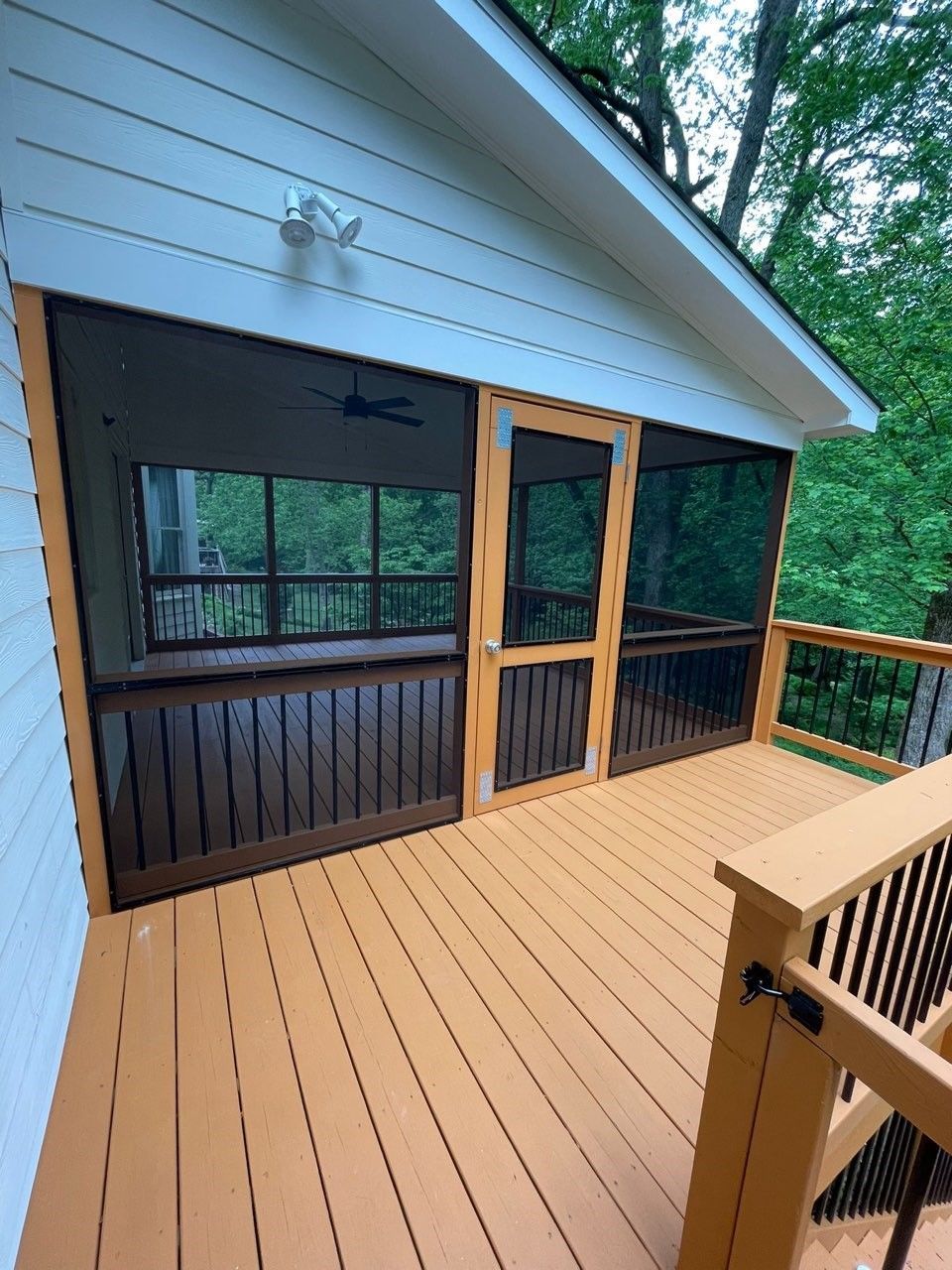 A screened in porch with a wooden deck and trees in the background.