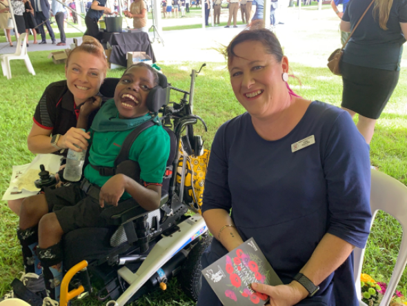 A man in a wheelchair is sitting on the grass with two women.