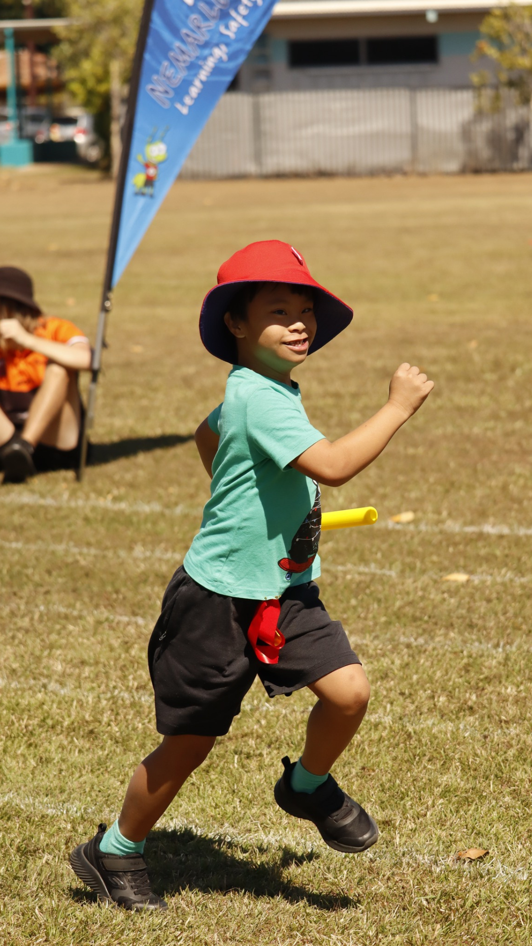 A young boy wearing a red hat is running on a field.