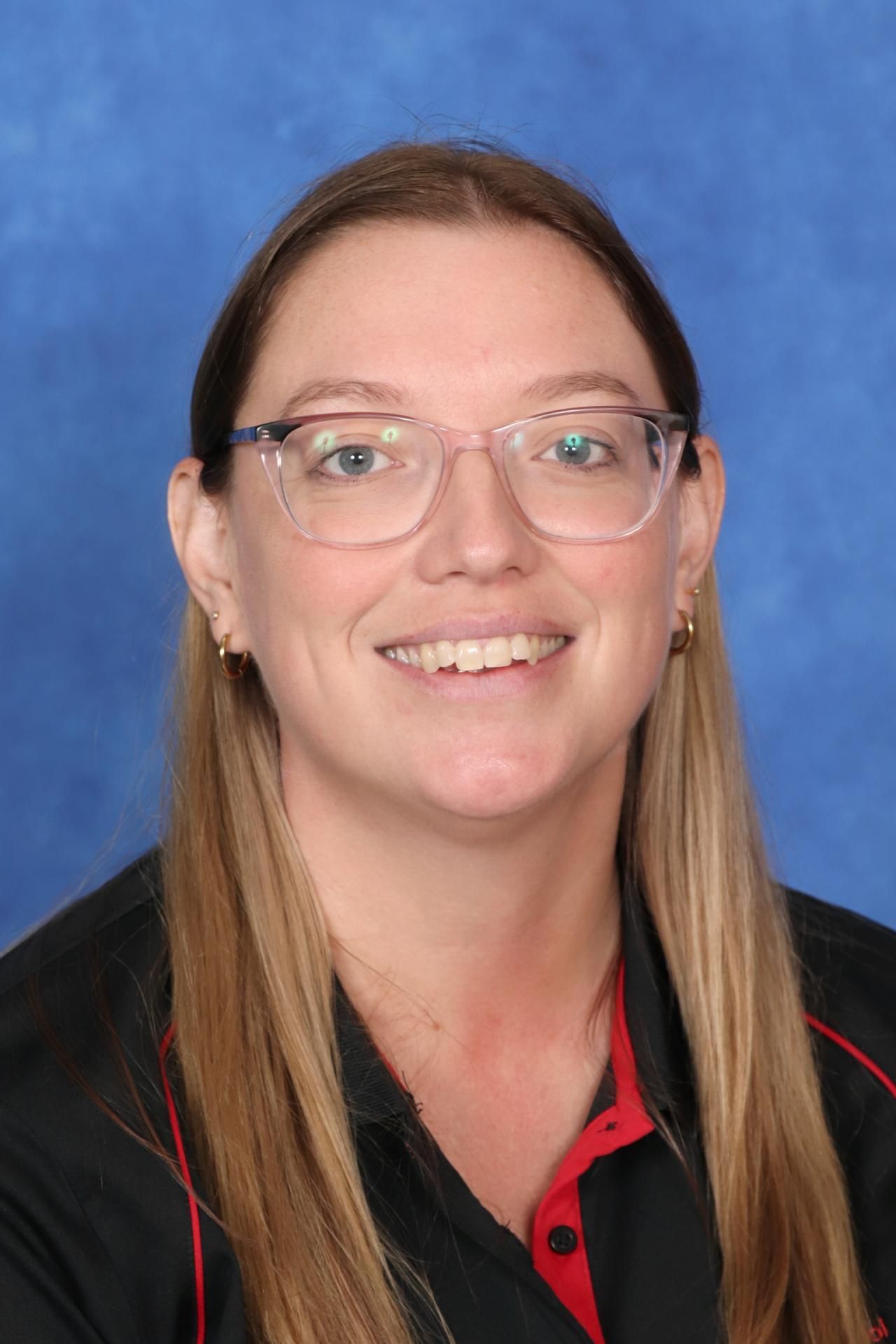 A woman wearing glasses and a red apron is smiling in front of a blue background.