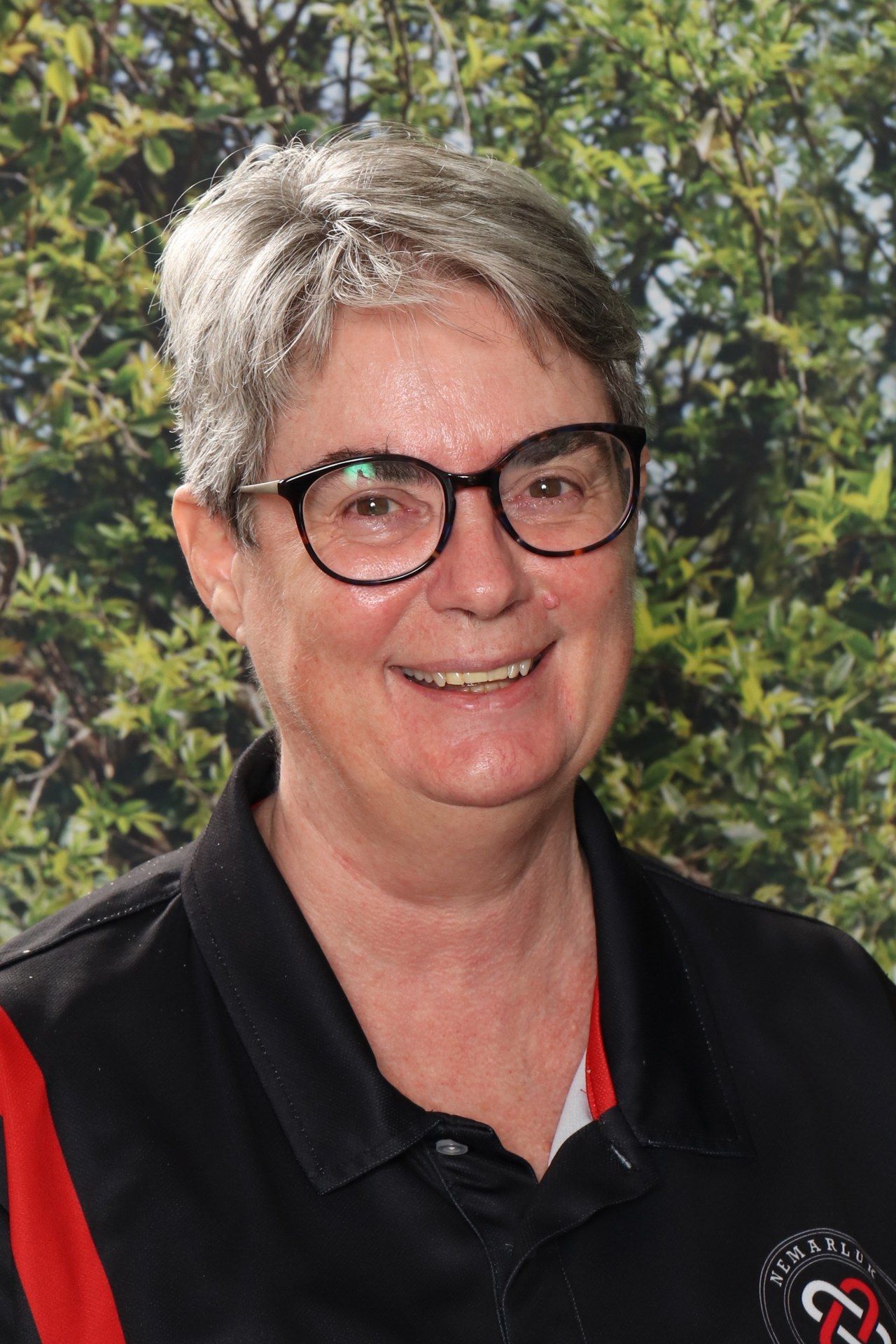 A woman wearing glasses and a black and red shirt is smiling for the camera.