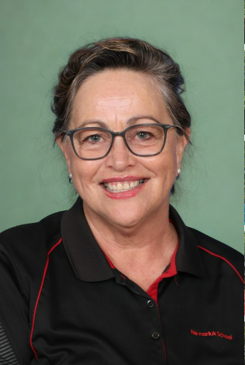 A woman wearing glasses and a red apron is smiling in front of a blue background.