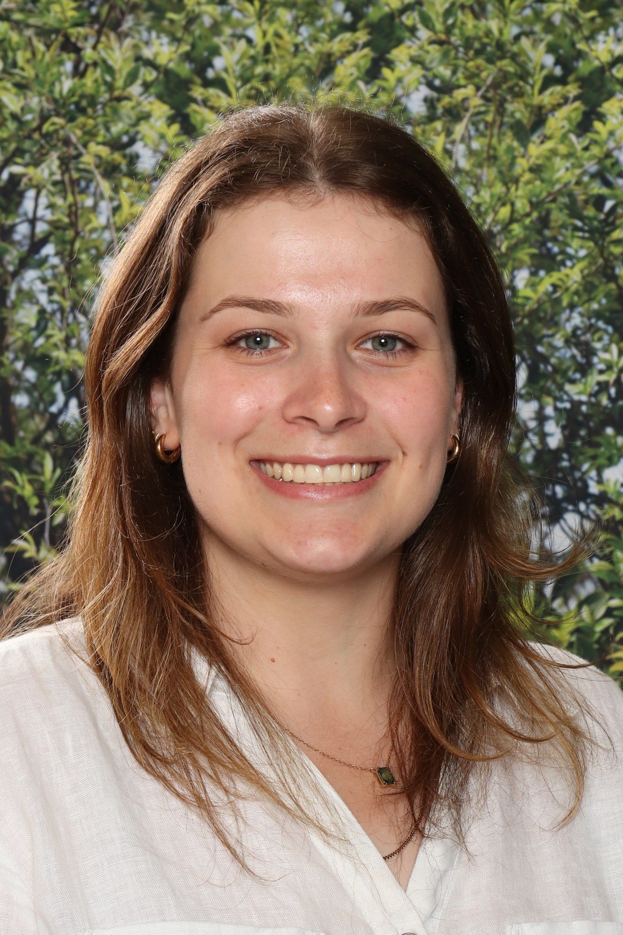 A woman wearing a floral shirt and a necklace is smiling in front of a blue background.