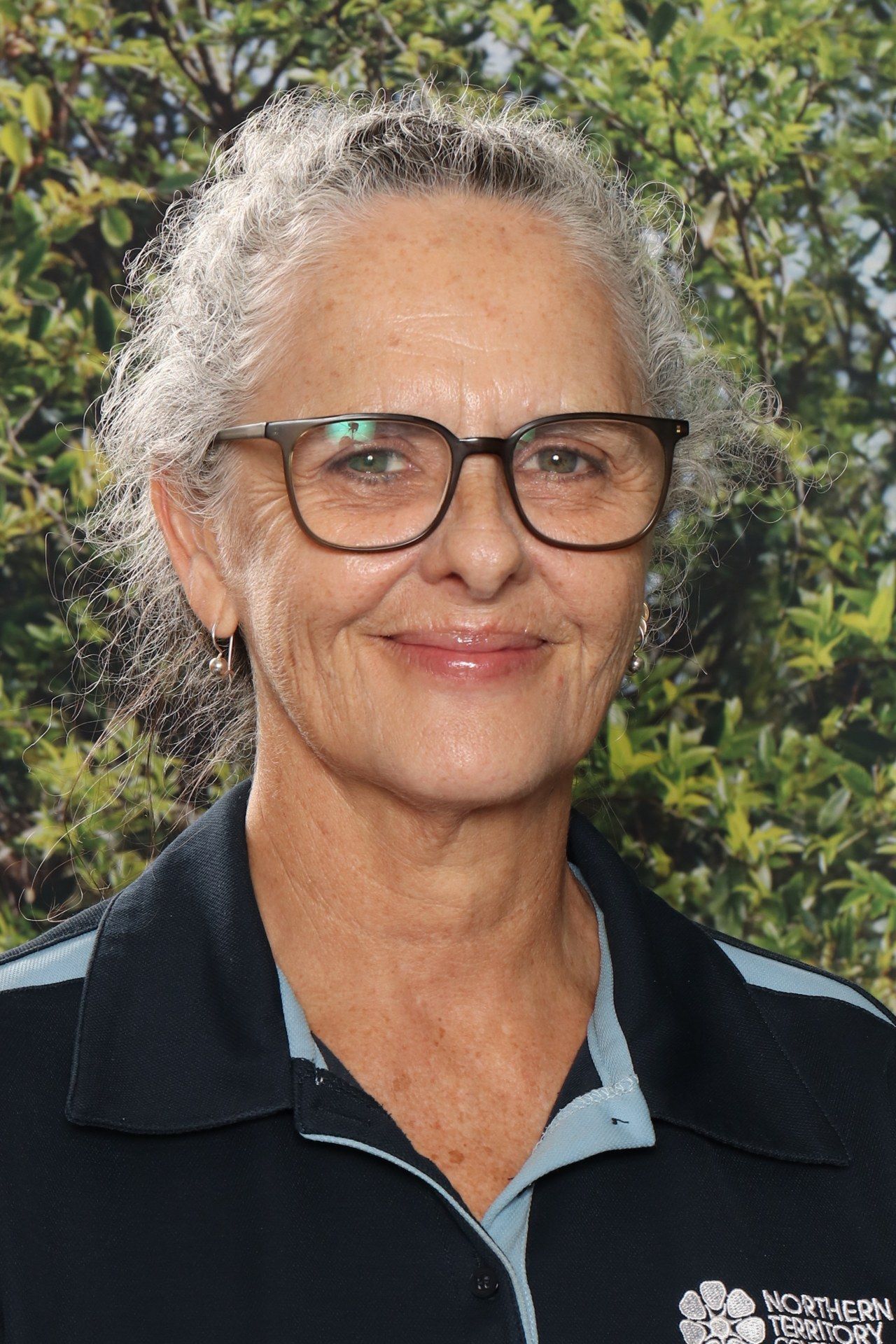 A woman in a blue shirt is smiling in front of a blue background.