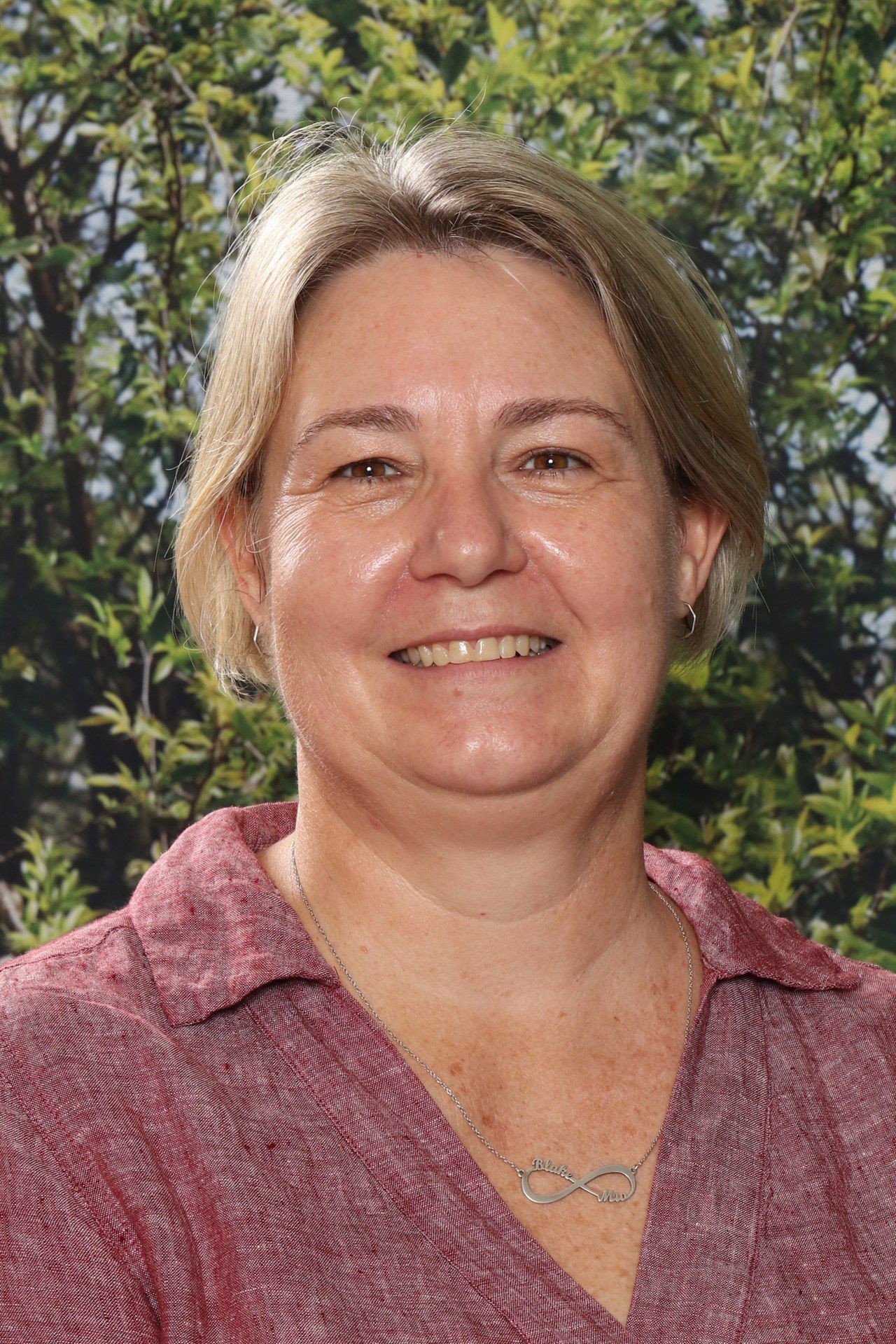A woman in a black shirt is smiling in front of a blue background.
