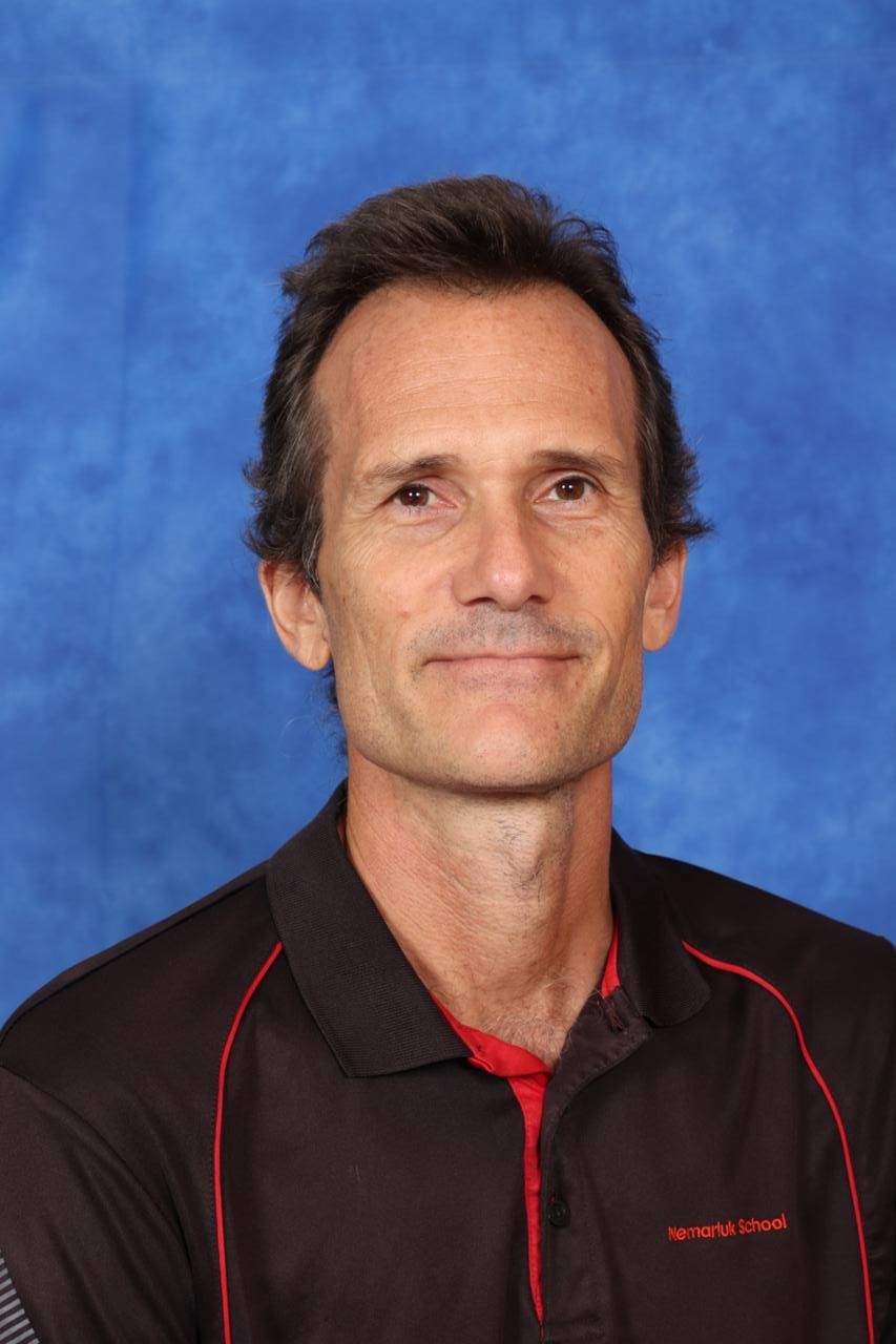 A man in a black and red shirt is standing in front of a blue background.