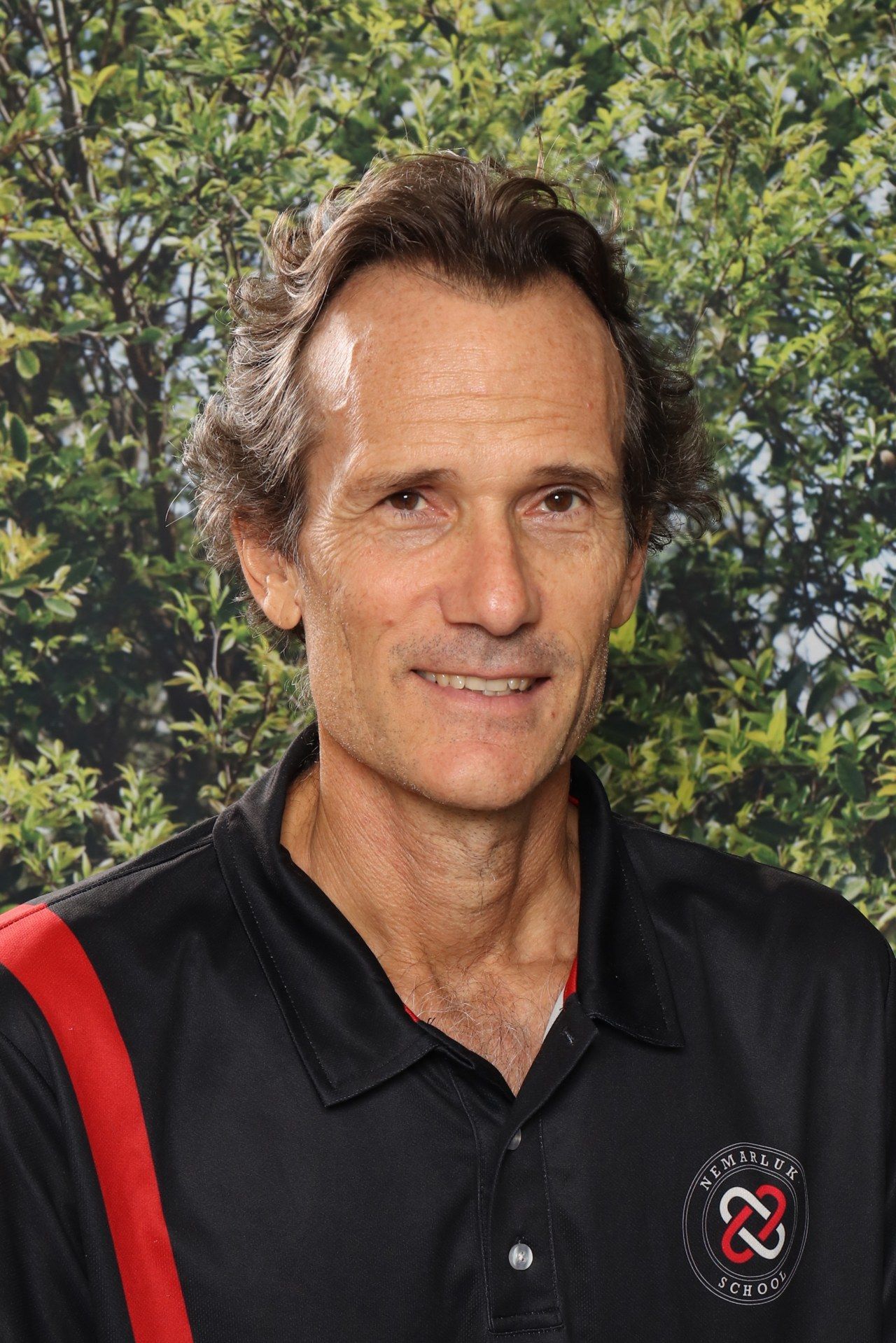 A man in a black and red shirt is standing in front of a blue background.