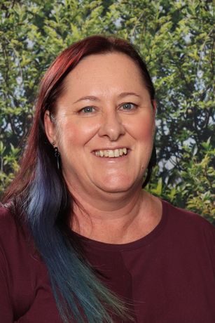 A woman with long black hair is smiling in front of a yellow wall.