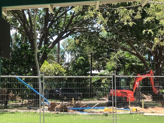 A red excavator is behind a fence in a park.