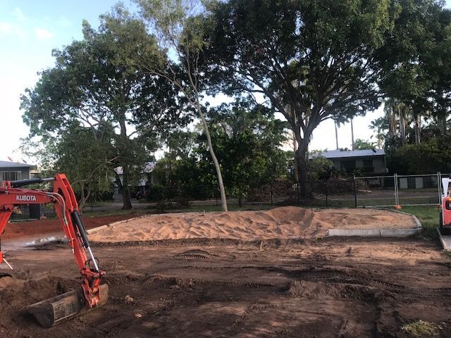 A red excavator is digging a hole in the dirt in front of a house.