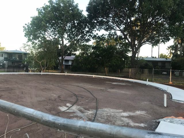 A fence surrounds a dirt field with trees in the background