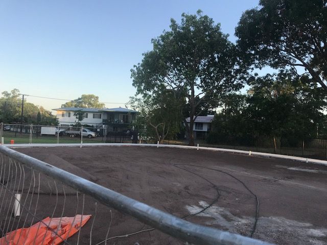 A fence surrounds a dirt field with a house in the background