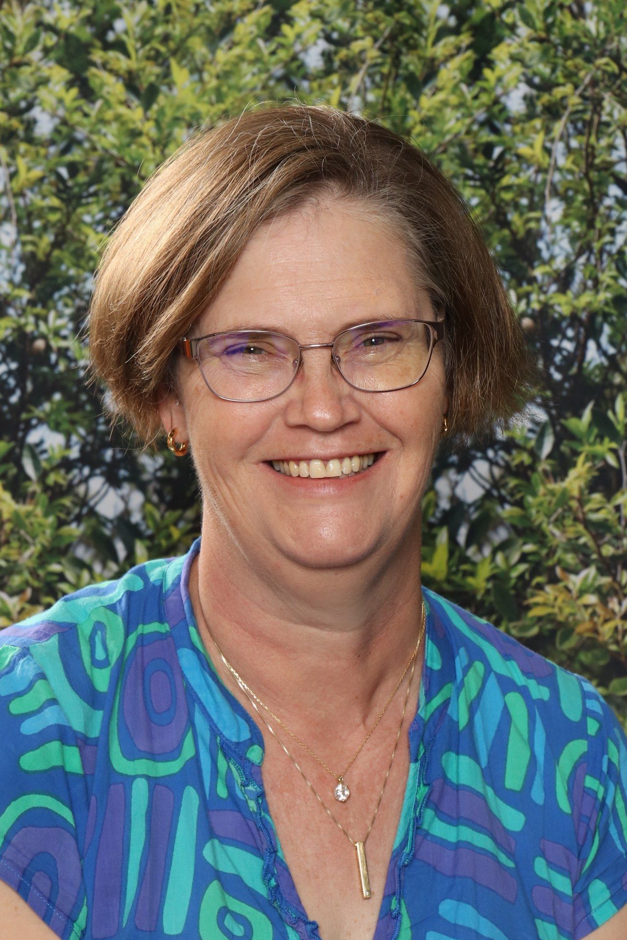 A woman wearing glasses and a red shirt is smiling for the camera.
