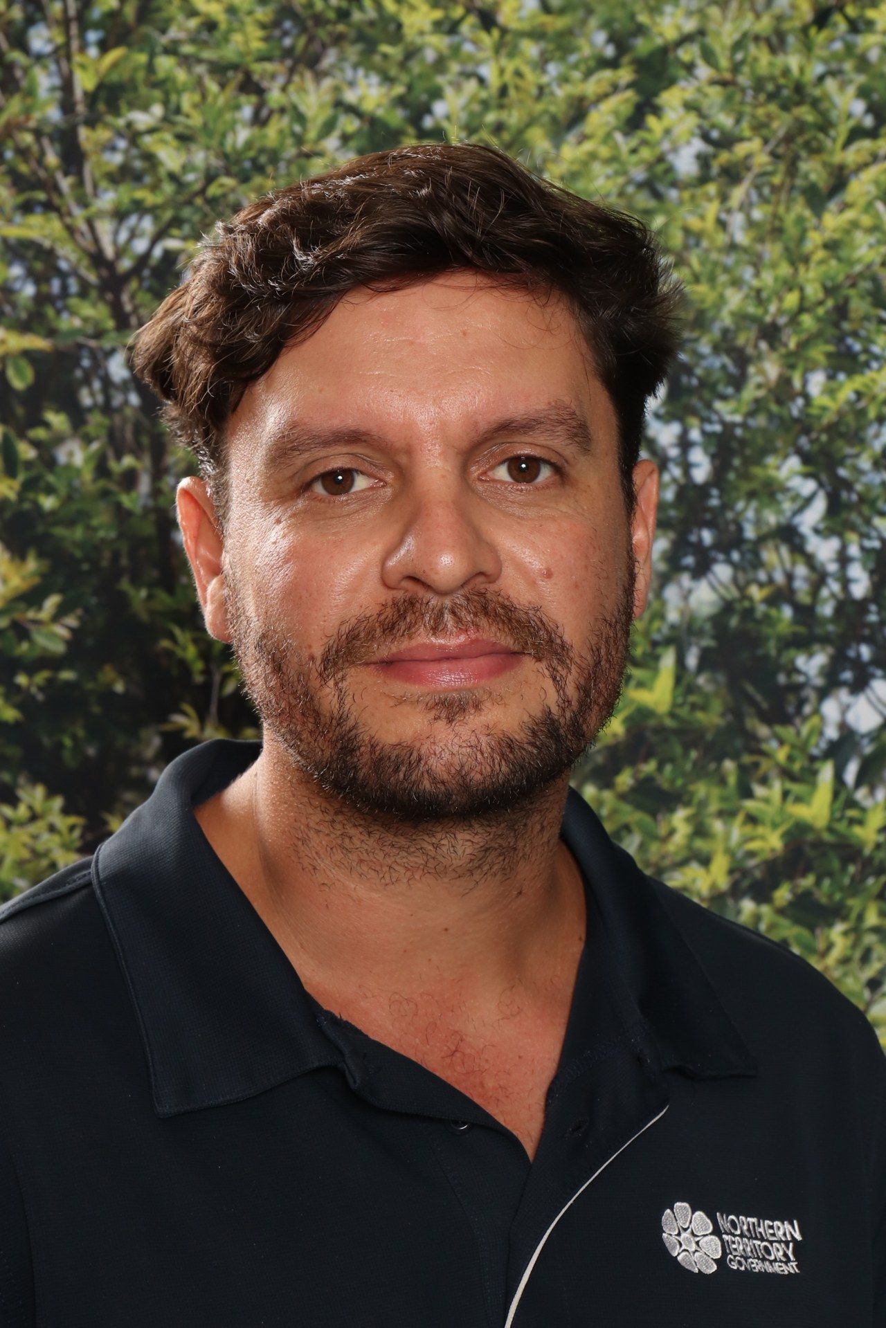 A man with a beard is smiling for a picture in front of a blue background.