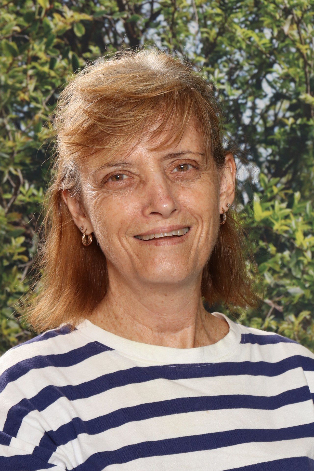 A woman in a red shirt is smiling in front of a blue background.